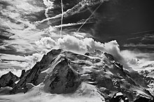 Photo noir en blanc d'une montagne couverte de neige et de glaciers avec des traînées de nuages et d'avions dans le ciel.