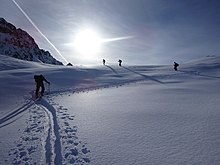 Skieurs de randonnée ayant fait une trace en Z dans de la poudreuse, sous un soleil éblouissant.