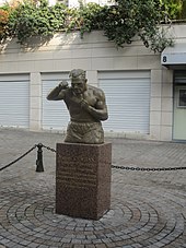 Statue avec un buste et un portrait, sur un socle sur lequel est célébré Marcel Cerdan, son palmarès et ses titres.
